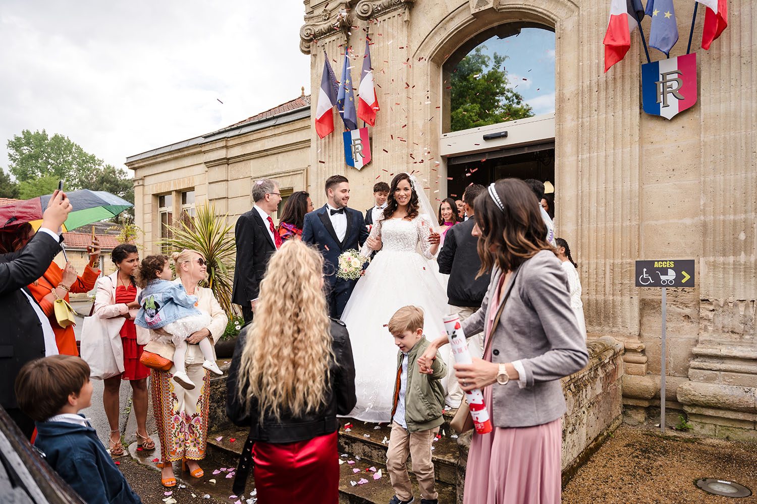 Photographie des mariés sous les confettis qui sont accueillis par leurs invités à la sortie de la mairie d'Ambarès-et-Lagrave.